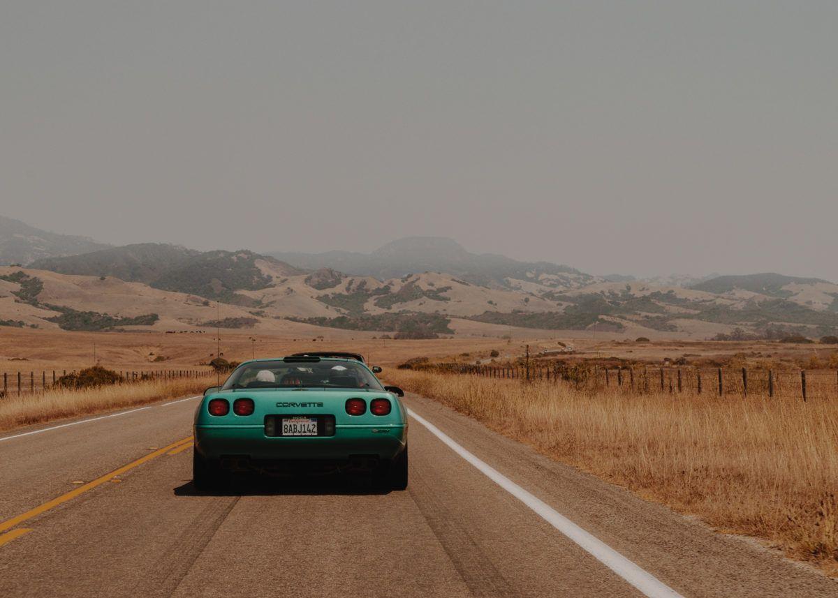 A classic green Corvette driving on a scenic highway surrounded by hills and dry grasslands, illustrating highway driving conditions.