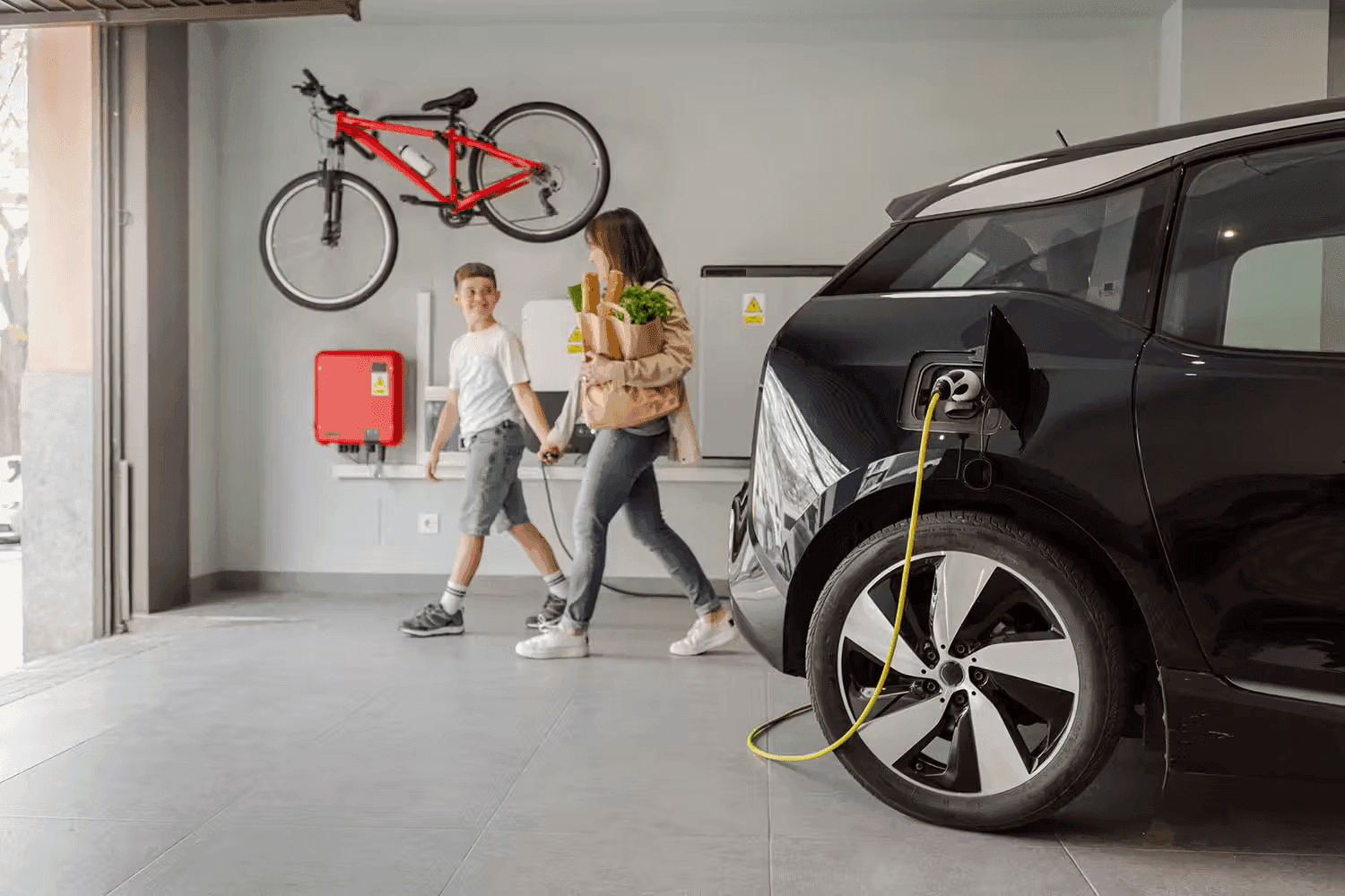A mother and son walking past a charging electric vehicle in a garage, showcasing a home EV charging setup and cost-saving benefits.