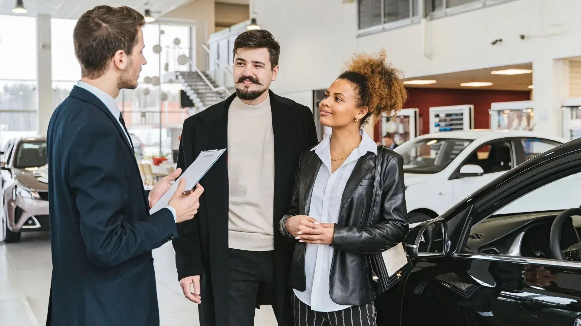 A couple discussing a used car purchase with a dealership salesperson, negotiating a price based on accident history.