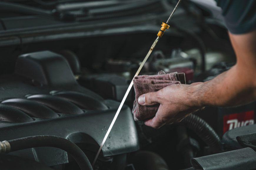 Person holding a dipstick with a clean rag to check the oil level in a car engine.