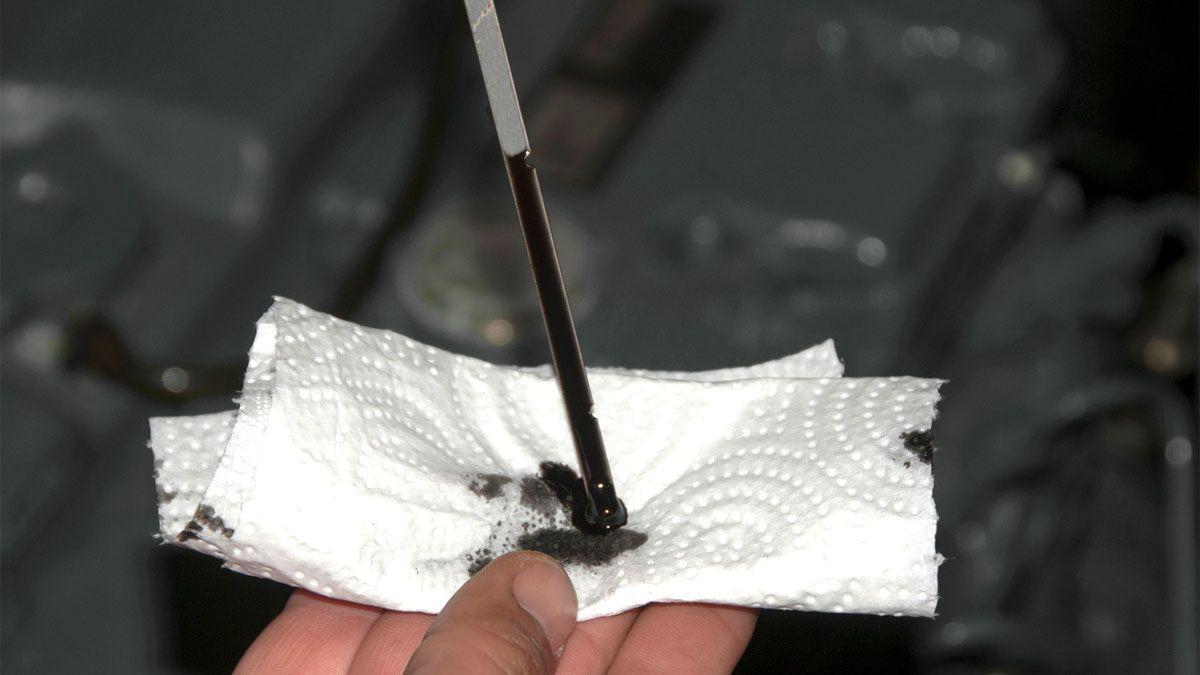 Close-up of a dipstick with dark, dirty engine oil, indicating the need for an oil change.