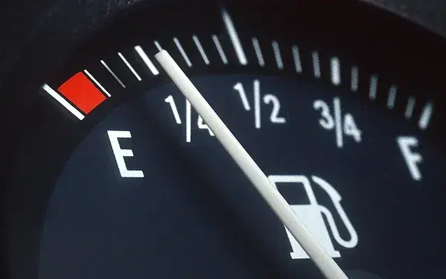 Close-up of a car fuel gauge showing low gas level, highlighting the importance of fuel efficiency for first-time drivers.