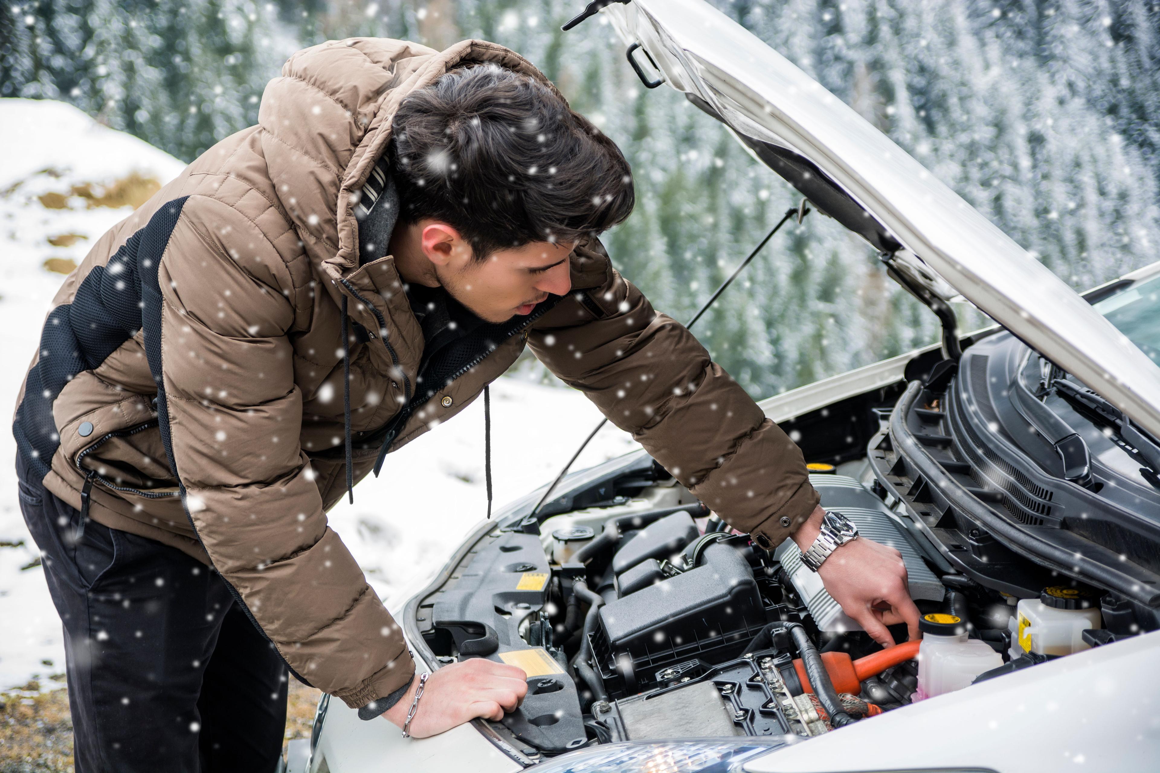 Man checking his car engine during winter to ensure it’s ready for cold weather.