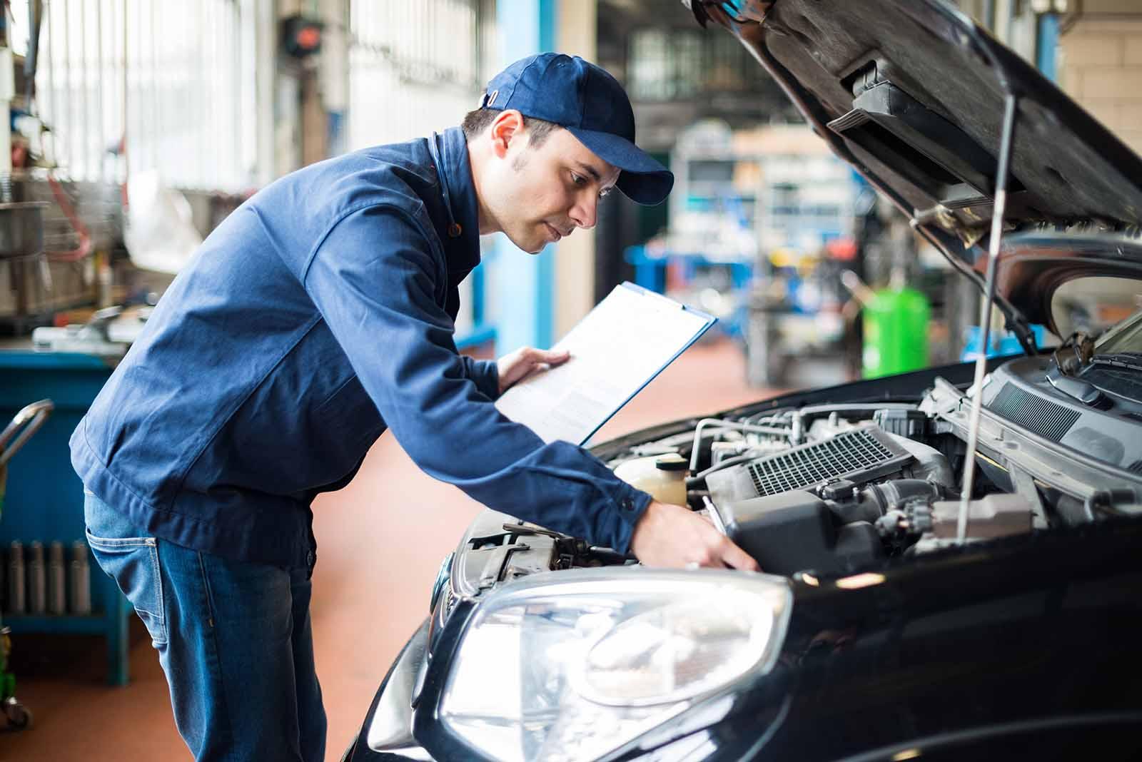 Mechanic inspecting a car engine with a clipboard, performing a maintenance check.