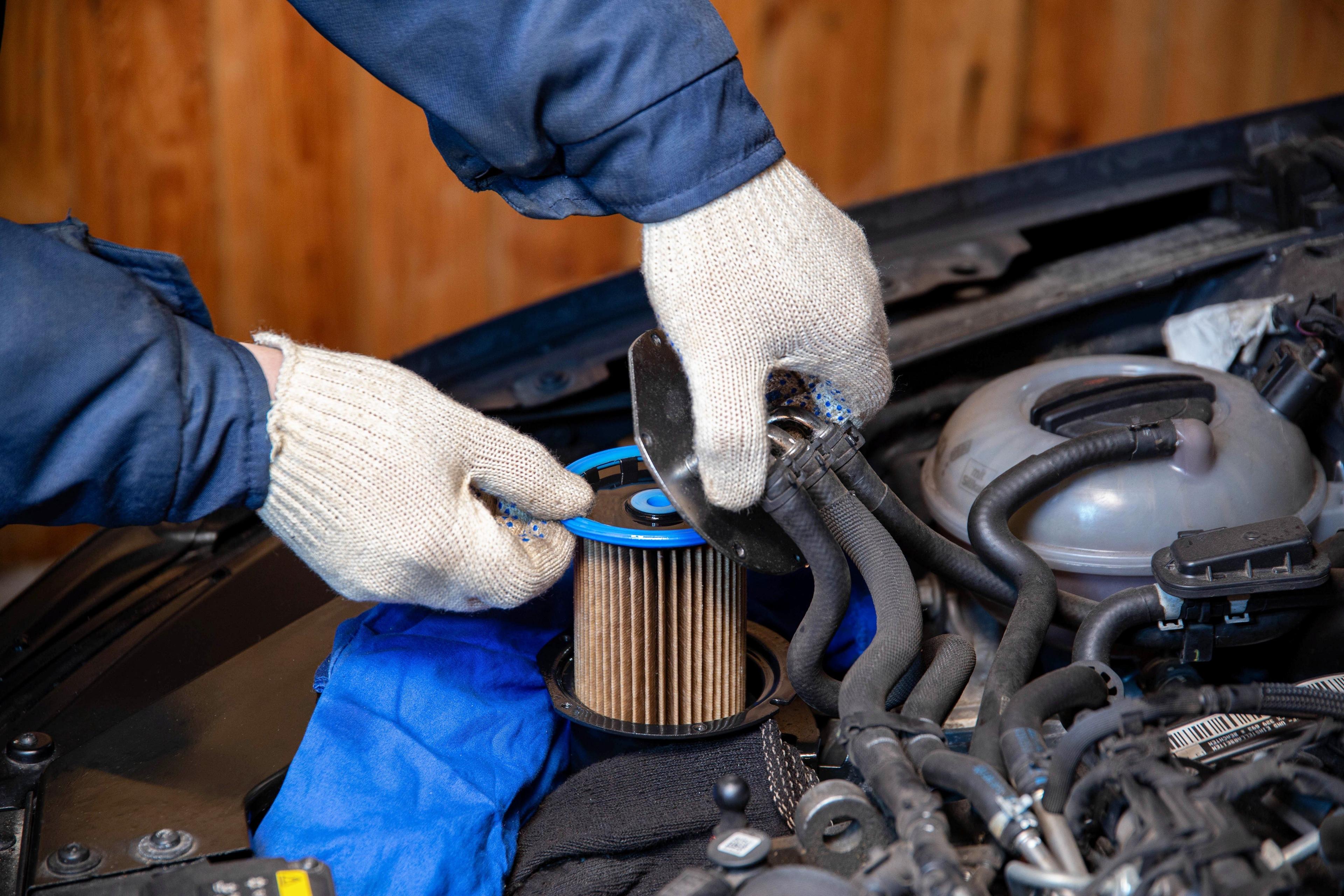 Mechanic wearing gloves installing a new fuel filter in a car engine.