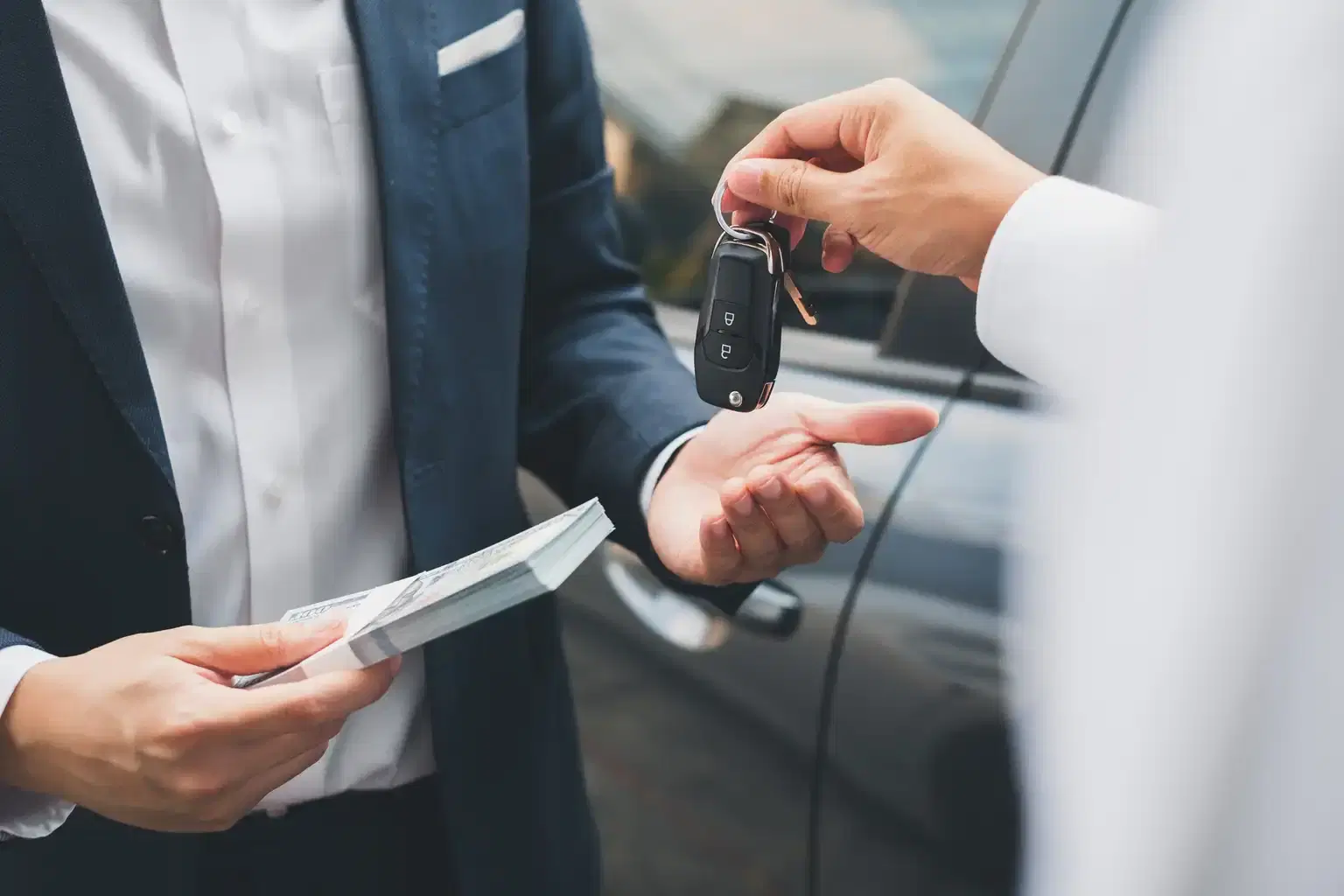 How to Sell a Car in California person handing car key to buyer holding cash beside a silver sedan on a sunny day