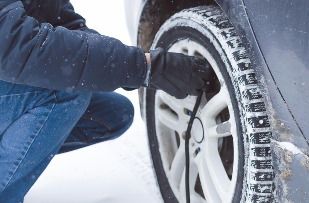 A person checking tire pressure during snowy conditions to ensure safe winter driving.